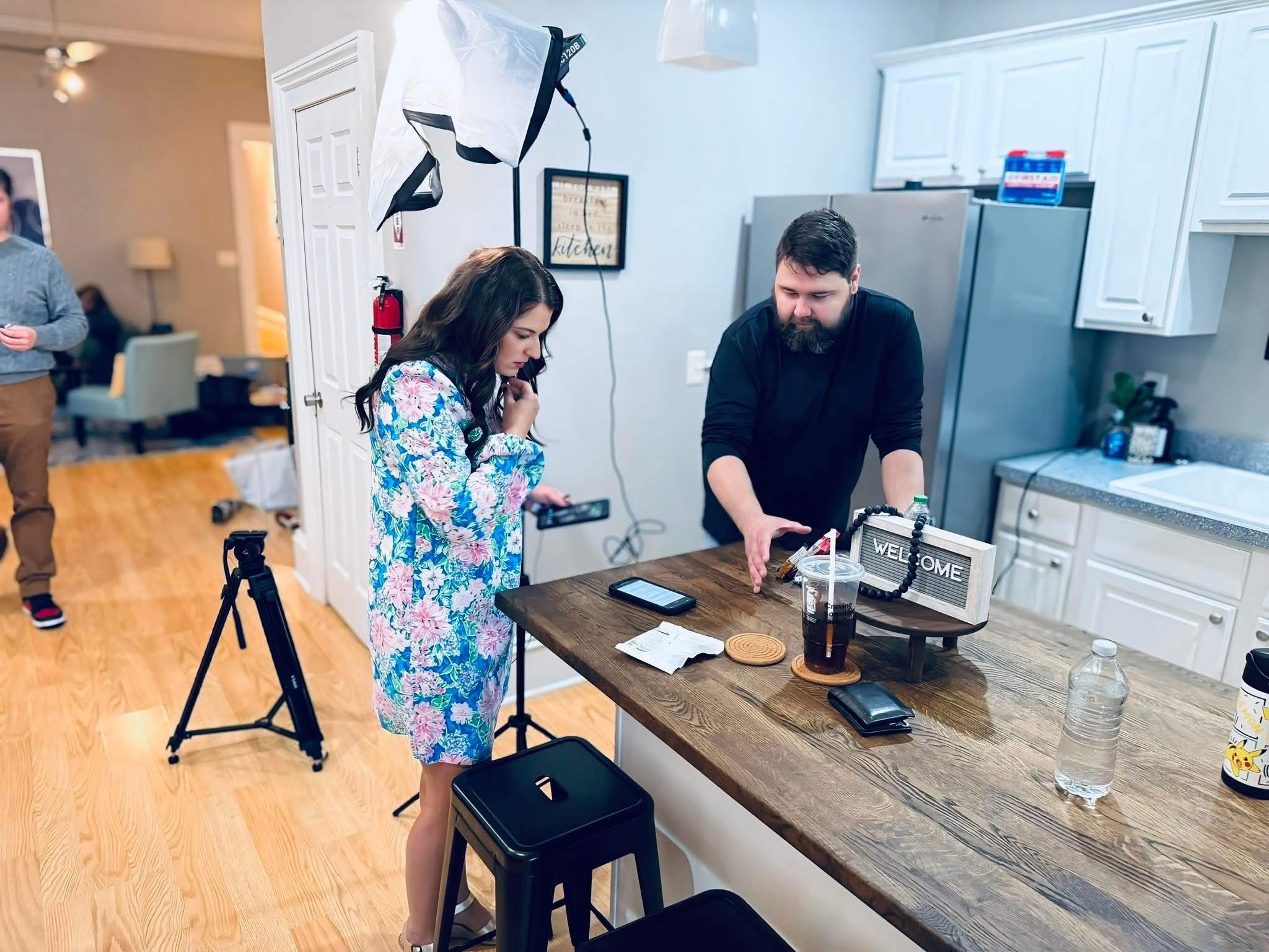 Behind the scenes — kitchen scene during principal photography, actress on phone, director setting a prop